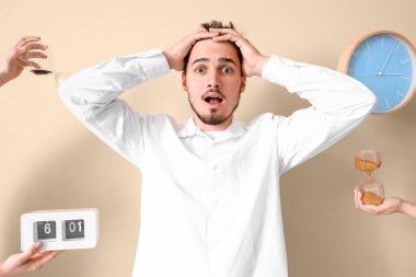 Stresli genç adam ve bej arka planda saatleri olan eller. Son teslim tarihi kavramı