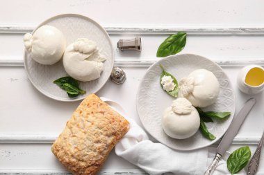 Lezzetli Burrata peyniri tabakları ve beyaz arka planda fesleğen ve ekmek.