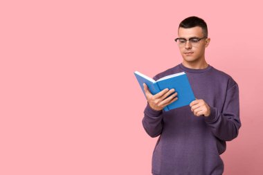 Yakışıklı genç adam pembe arka plan üzerine kitap okuyor.