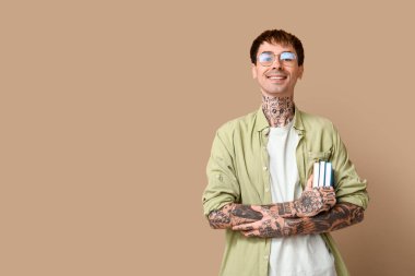 Kahverengi arka planda kitapları olan dövmeli genç bir adam.