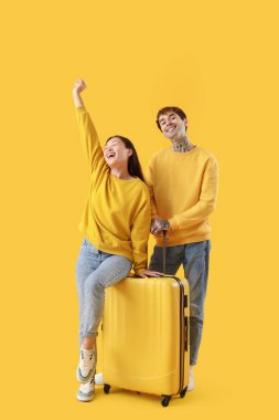 Sarı arka planda bavulu olan genç gezginler.