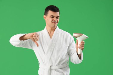 Fotokopi makinesi olan genç adam yeşil arka planda baş parmağını aşağı gösteriyor.