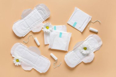 Tamponlu regl pedleri ve bej arka planda kasımpatı çiçekleri.