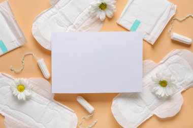 Regl pedleri, tamponlar ve bej arka planda kasımpatı çiçekleri olan boş bir kağıt.
