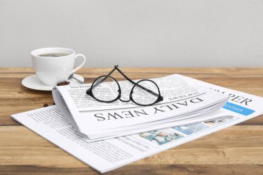 Bardaklı gazeteler ve ahşap masada bir fincan kahve.