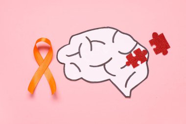 Kağıt beyin, bulmaca parçaları ve pembe arka planda turuncu kurdele. Çoklu Skleroz Farkındalık Ayı