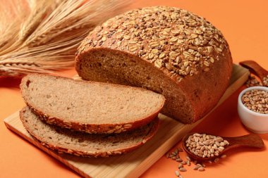 Turuncu arka planda dilimlenmiş somun ekmek, tohum ve buğday dikenli tahta.