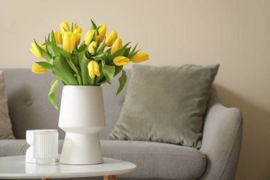 Gri kanepesi ve kahve masasında sarı laleleri olan modern oturma odası.