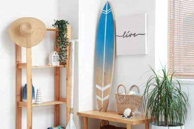 Surfboard, picture, bag and paddle near white wall in room