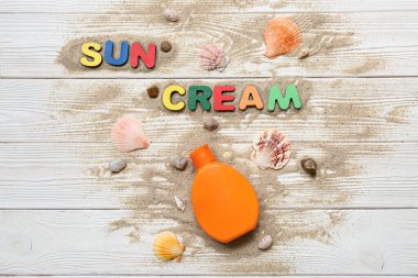 İfade: Güneş kremi, bir şişe güneş kremi, deniz kabukları ve ahşap zemin üzerinde kum