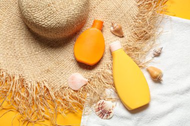 Hasır şapka, güneş kremi şişeleri, havlu ve deniz kabukları.