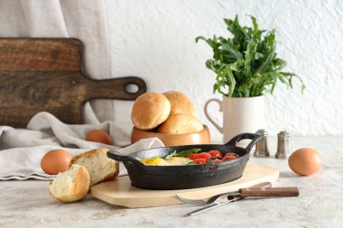 Lezzetli yumurtalı tava, domates ve çörekler hafif masada.