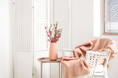 Işık odasındaki koltuğun yanındaki kahve masasında Sakura çiçekli vazo.