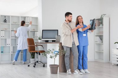 Kadın doktor, hastanede genç bir adama ciğerlerinin röntgenini gösteriyor.