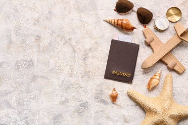 Pasaport, güneş gözlüğü, ahşap uçak ve arka planda deniz kabukları olan kompozisyon