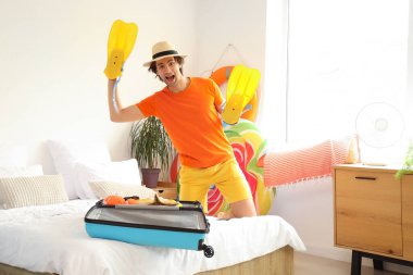 Paletli ve bavullu mutlu erkek turist tatilde yatak odasında.