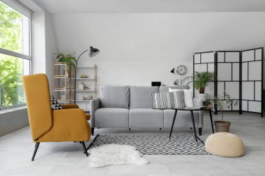 Gri kanepeli, masalı ve koltuklu aydınlık oturma odasının içi.