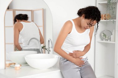 Genç Afro-Amerikalı kadın banyoda regl sancısı çekiyor.