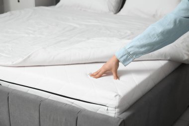 Evdeki yatakta yumuşak ortopedik şilteye dokunan kadın, yakın plan.