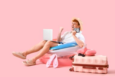 Pembe arka planda dizüstü bilgisayarı ve plaj aksesuarları olan genç adam.