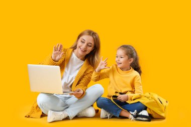 Küçük liseli kız ve dizüstü bilgisayarı olan büyükannesi sarı arka planda sohbet ediyorlar.