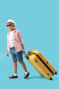 Mavi arka planda bavulu olan, güneş gözlüklü ve şapkalı Afro-Amerikalı bir çocuk. Seyahat kavramı