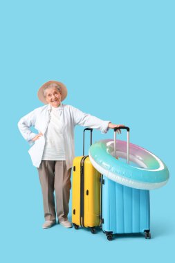 Bavulları ve mavi arka planda yüzen yaşlı bayan turist.