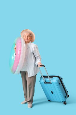 Mavi arka planda yüzme yüzüğü ve bavulu olan son sınıf bayan turist.