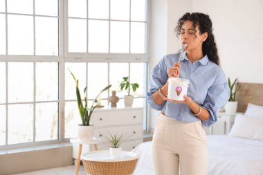 Yatak odasında bir sepet dondurması olan güzel bir Afro-Amerikalı kadın.