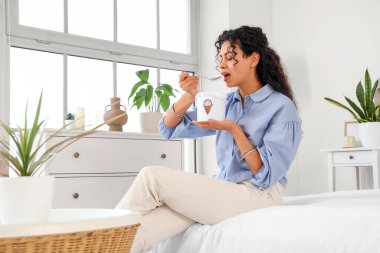 Güzel, Afro-Amerikalı bir kadın dondurma yiyor ve evde yatakta oturuyor.