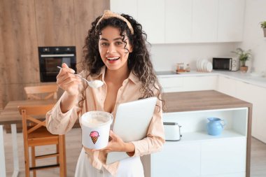 Mutfakta bir sepet dondurma ve modern dizüstü bilgisayarı olan güzel bir Afro-Amerikalı kadın.