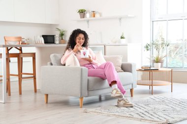 Evdeki kanepede oturan bir sepet dondurmalı güzel Afro-Amerikalı kadın.