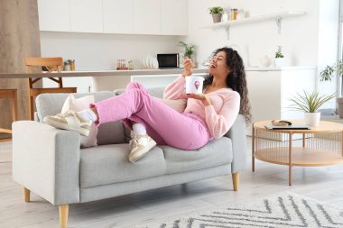 Evdeki kanepede uzanmış bir sepet dondurmayla güzel bir Afro-Amerikalı kadın.