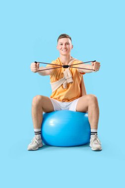 Sportif genç adam mavi arkaplana karşı fitbalda genişletici ile