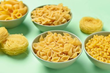 Yeşil arka planda farklı pişmemiş makarna kaseleri, yakın plan.