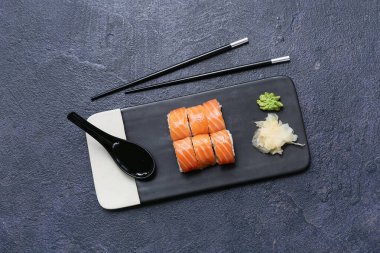 Lezzetli suşi ruloları, yemek çubukları ve siyah grunge arka planda kaşık.