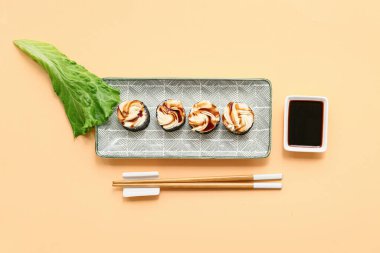 Lezzetli suşi ruloları, yemek çubukları ve bej arka planda soya soslu tabak.