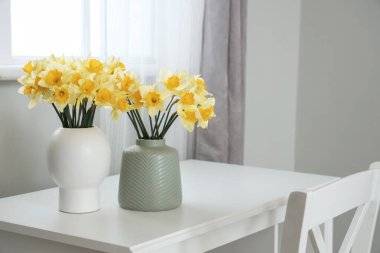 Masa ve vazolar Narcissus çiçekleriyle dolu odada.