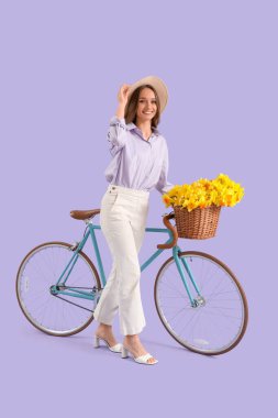 Leylak arka planında nergis ve bisikleti olan güzel genç bir kadın.