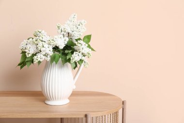 Odadaki bej duvarın yanındaki sehpanın üzerinde çiçek açan dalları olan vazo.