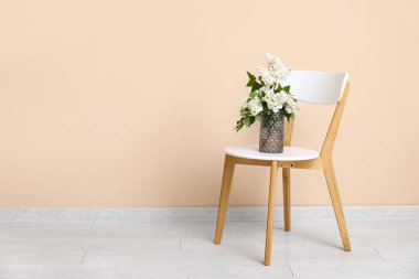 Odadaki bej duvarın yanındaki sandalyenin üzerinde çiçek açan dalları olan vazo.