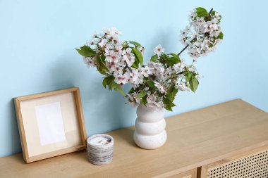 Mavi duvarın yanındaki masada çiçek açan dalları olan bir vazo.