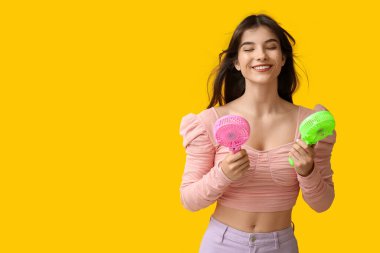 Sarı arka planda mini fanları olan genç bir kadın.