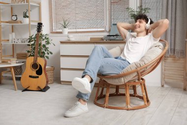 Kulaklıklı yakışıklı genç adam evdeki koltukta müzik dinliyor.