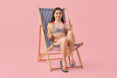 Güneş kreminden yapılmış genç bir kadın pembe arka planda iskemlede oturuyor.