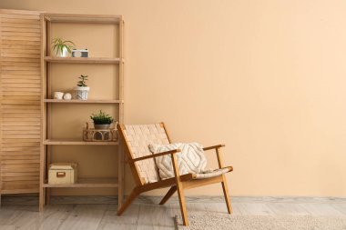 Bej duvarın yanında raf ünitesi ve koltuğu olan şık bir oturma odası.