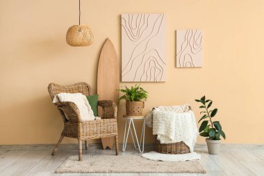 Hasır koltuğu, sörf tahtası ve bej duvarda asılı resimleri olan şık bir oturma odası.