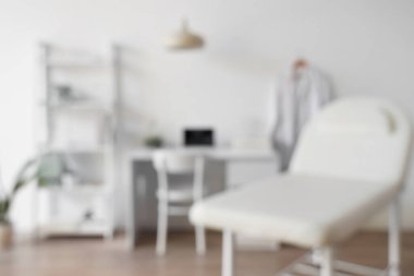 Kanepesi, doktor çalışma yeri ve raf ünitesi olan bulanık tıbbi ofis manzarası.