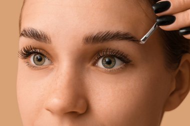 Kahverengi arka planda kaşlarının şeklini düzelten genç bir kadın, yakın plan.