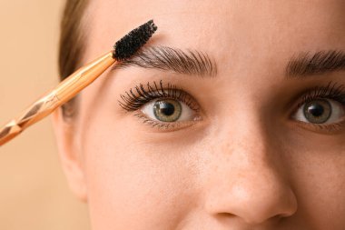 Kahverengi arka planda kaşlarının şeklini düzelten genç bir kadın, yakın plan.